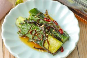 器に盛られた和風ピクルス、キュウリと赤唐辛子、ゴマがトッピングされた料理。背景にガラス容器に入った同料理。