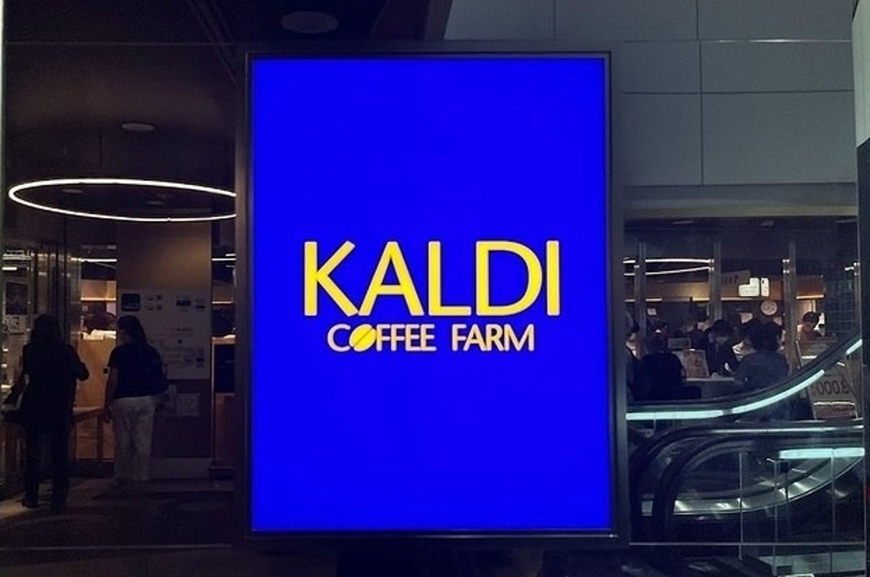 青い看板に「KALDI COFFEE FARM」と表示されているショップサイン。店内の様子が背景に映っている。