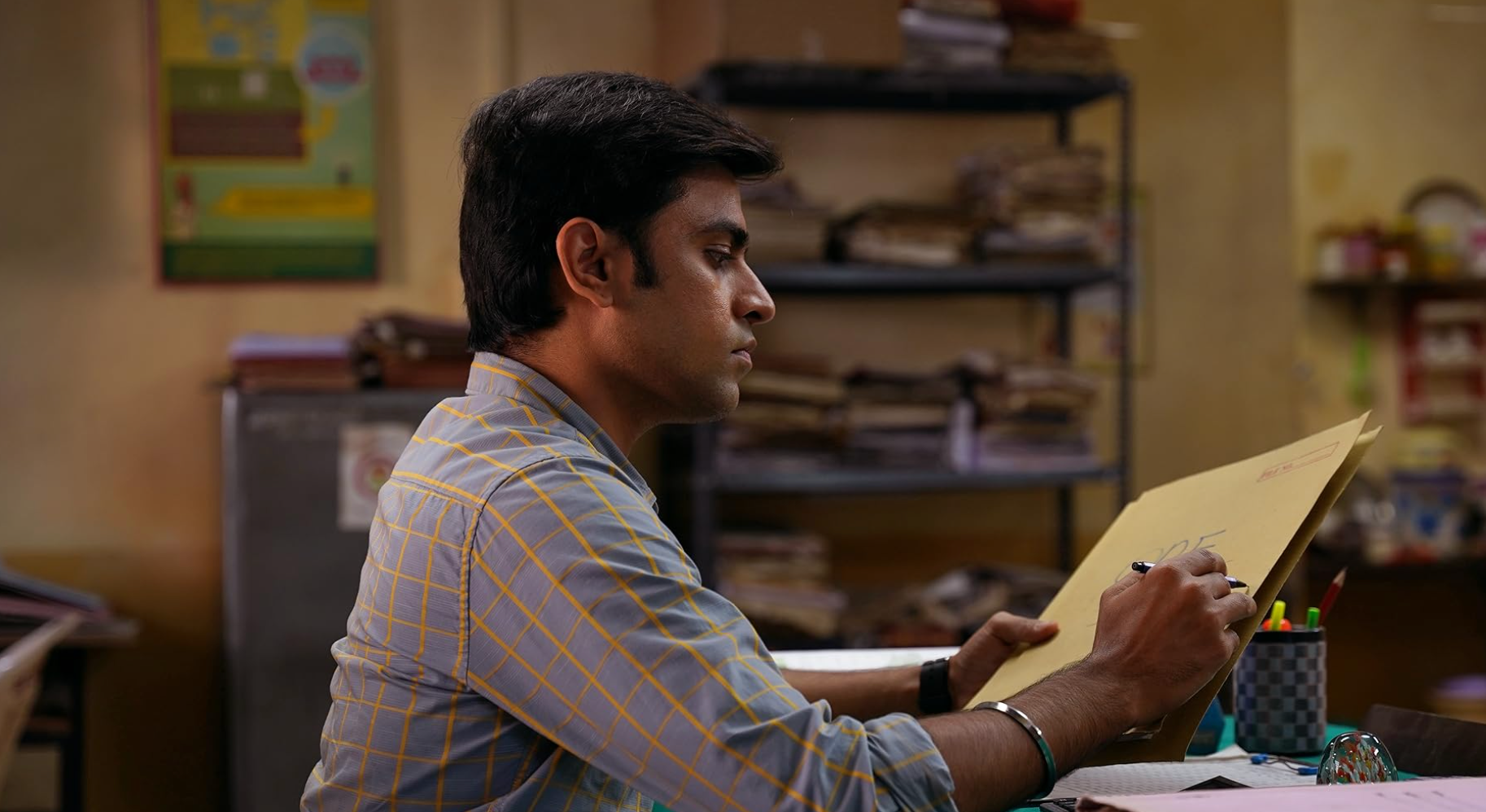 Person sitting at a desk, holding a large envelope, surrounded by office supplies and paperwork in a cozy office setting