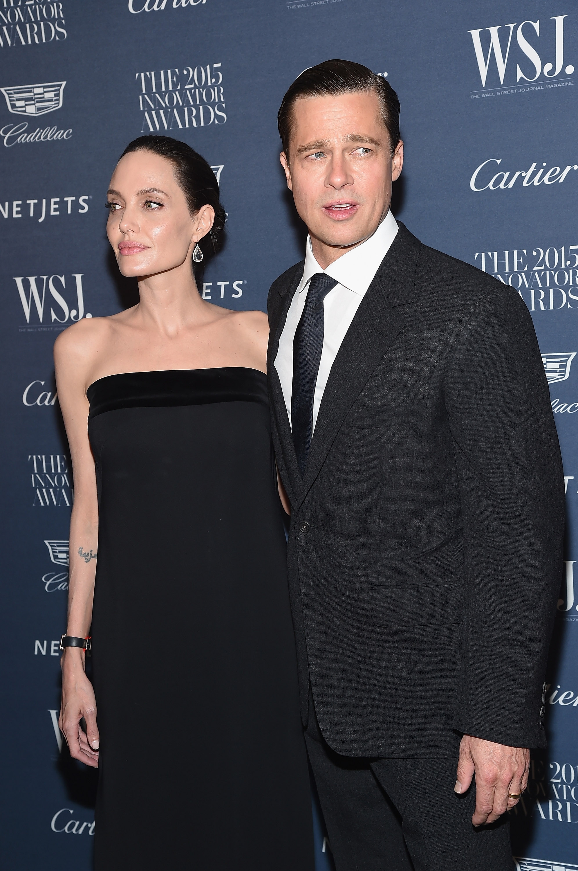Two individuals in formal attire at an event. One wears a strapless dress and the other a suit and tie, posing on the red carpet