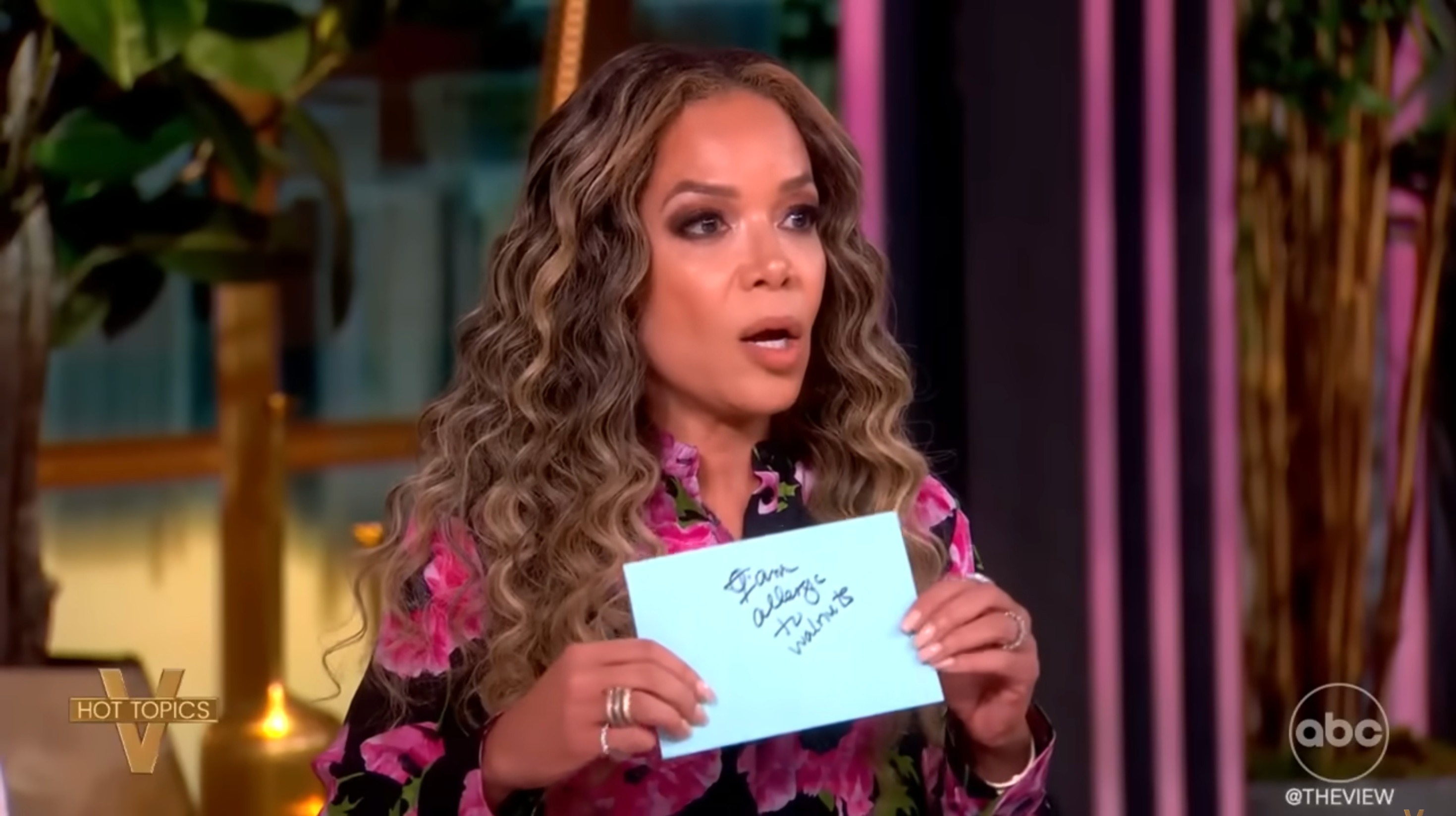 Person on a talk show holding a card with handwritten text, likely making a point during a discussion