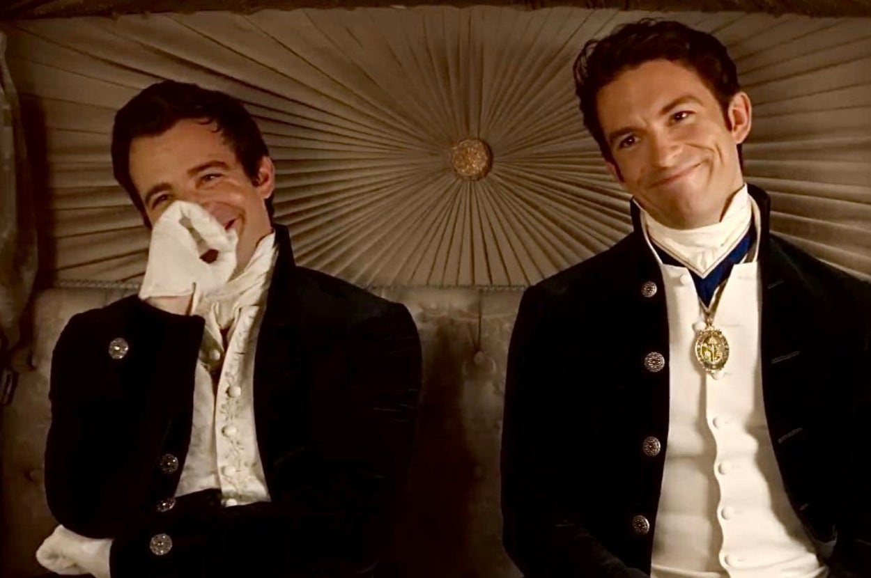 Two men in period costumes sit in a carriage, laughing. Their outfits feature ornate details and high collars