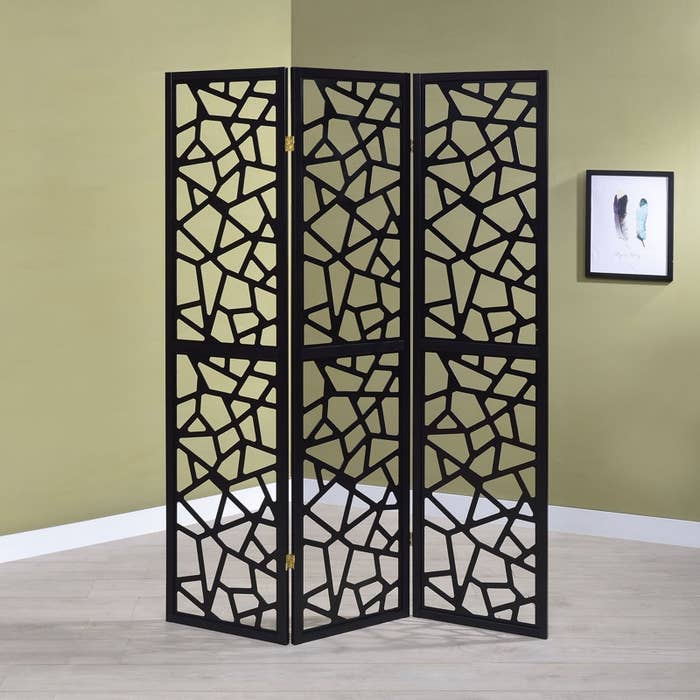 Room divider with geometric cut-out panels stands against an bare wall. Modern and decorative, perfect for adding benignant to a space