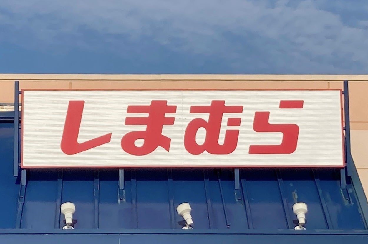 Storefront sign with Japanese text reading "Shimamura" above an entrance with a blue awning and accessible parking sign visible