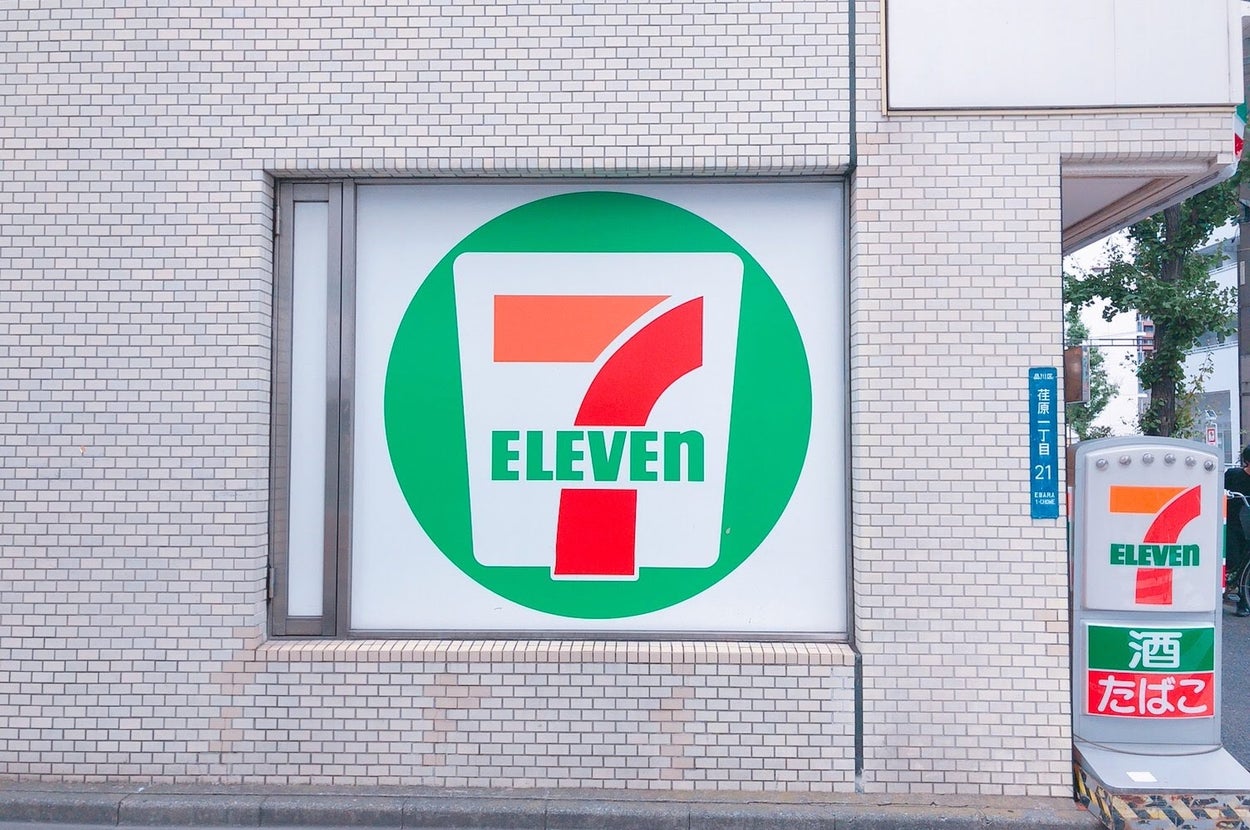 セブンイレブンの大きなロゴが店舗の外壁に表示されている。左に自販機が立っている。