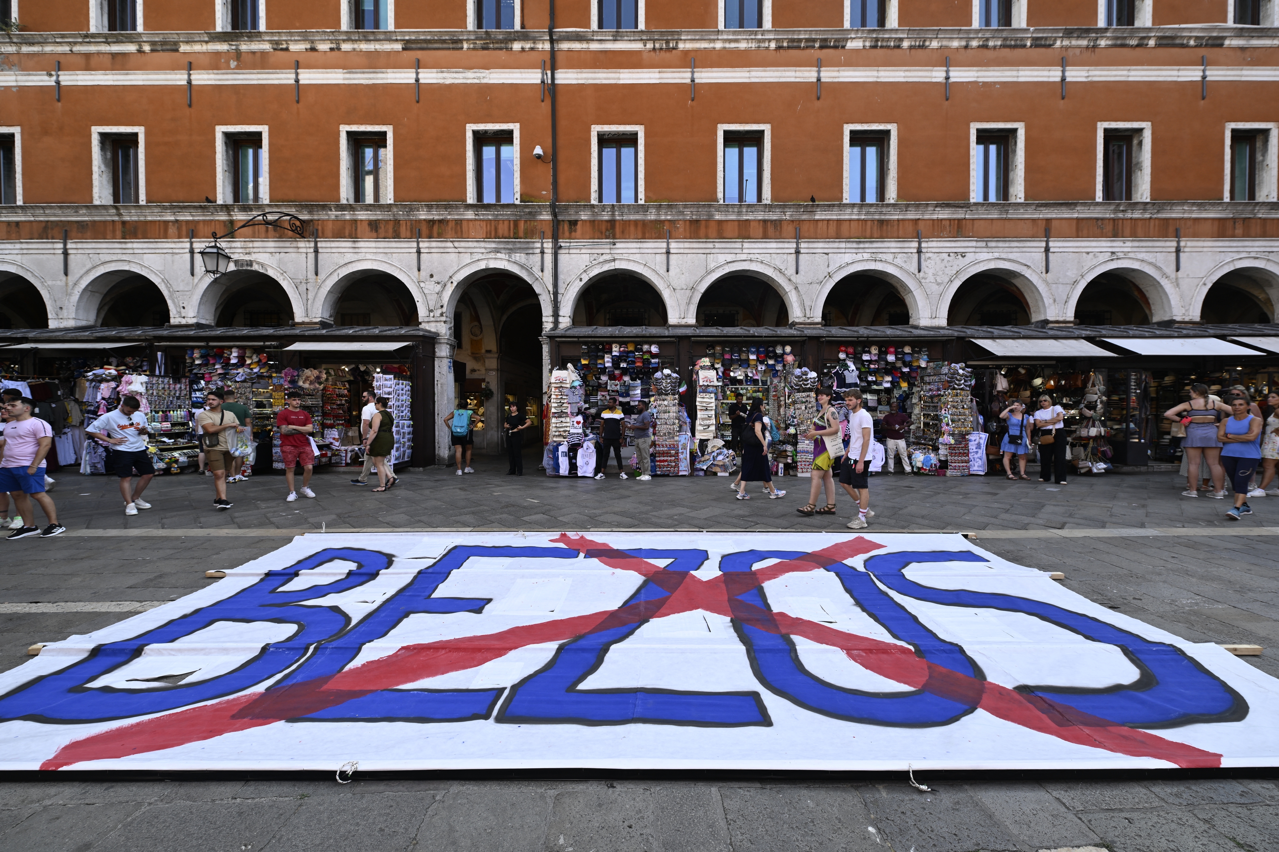 Large banner on the ground with &quot;BEZOS&quot; crossed out in red, displayed in a busy public square with people walking by