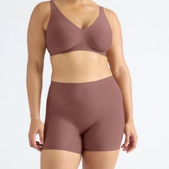 Person modeling seamless undergarments, including a bra and shorts, in a neutral setting