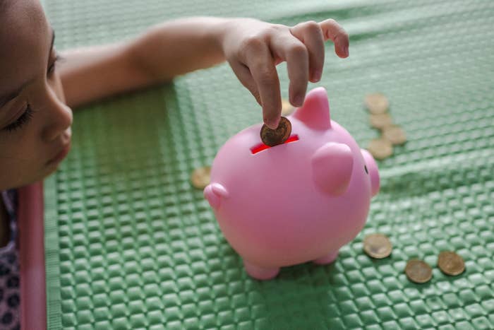 Child placing a coin into a piggy bank on a textured surface, with additional coins scattered around