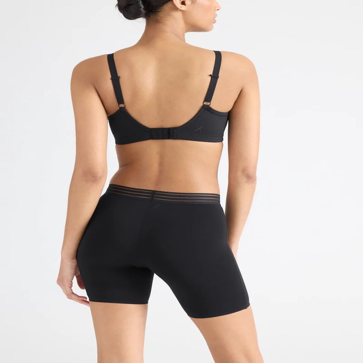 A person is wearing a black bra and high-waisted shorts, showcasing the fit and design of undergarments from the back view