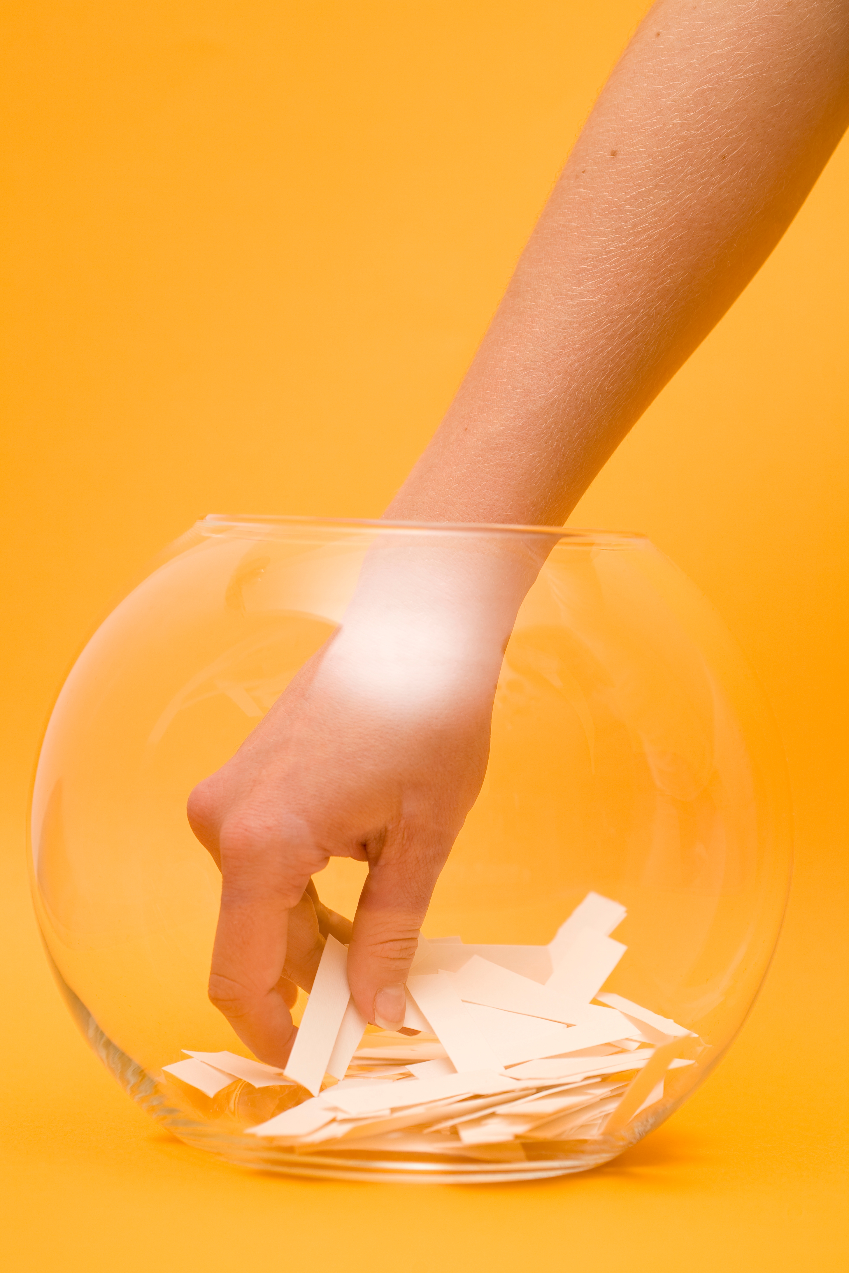 A hand reaches into a clear glass bowl filled with paper slips, presumably for a random selection or draw