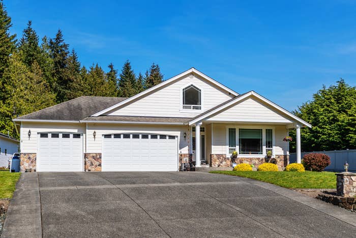 Single-story suburban location with 2 garages, a neatly maintained lawn, and surrounding trees connected a wide day
