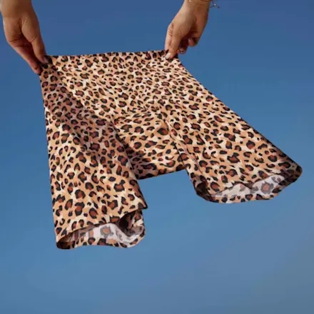 Person holding leopard-print cycling shorts against blue sky