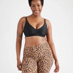Person wearing a black bra and leopard print shorts, smiling confidently. Fashionable and comfortable activewear showcased for shopping feature
