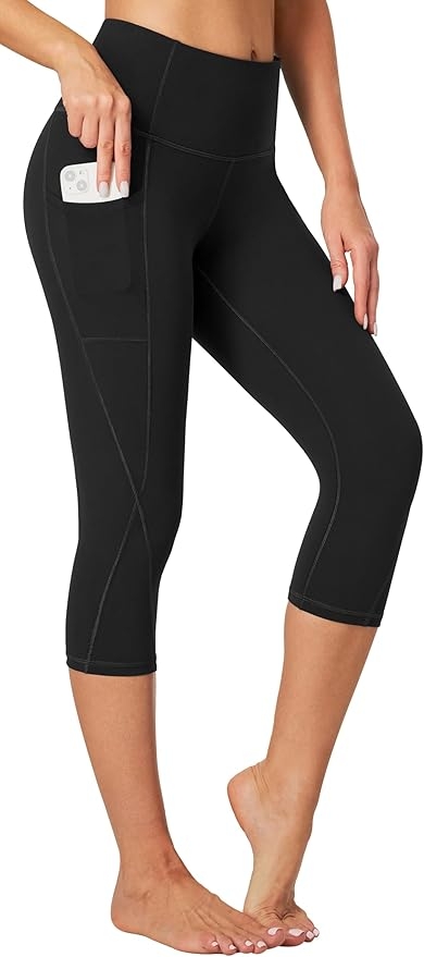 A person wearing black capri leggings with a pocket holding a phone. The focus is on the leggings' fit and pocket convenience