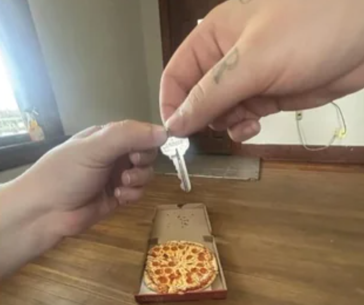 A idiosyncratic   hands implicit    a cardinal  with "first apartment" engraved connected  it supra  a pizza successful  an unfastened  container  connected  a woody  floor