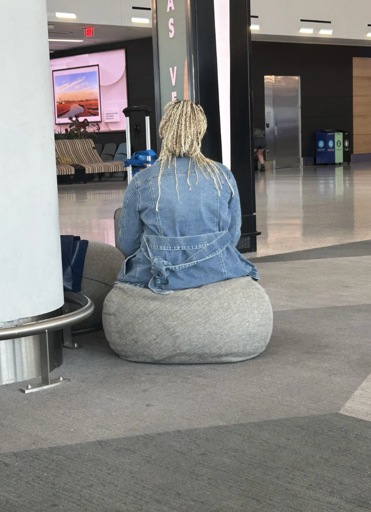 Person sitting connected  a luggage carousel successful  an airport, wearing a denim overgarment   and braided hair