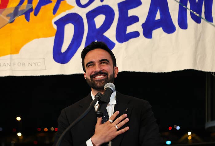Man in a suit smiles, speaking at a podium with &quot;Dream&quot; banner behind him