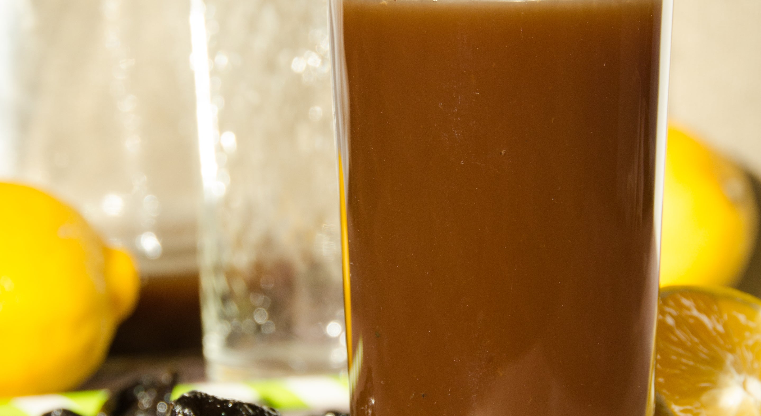 Glass sviskesaft på et bord med hele og halverte sitroner, svisker og en mynte kvist i nærheten