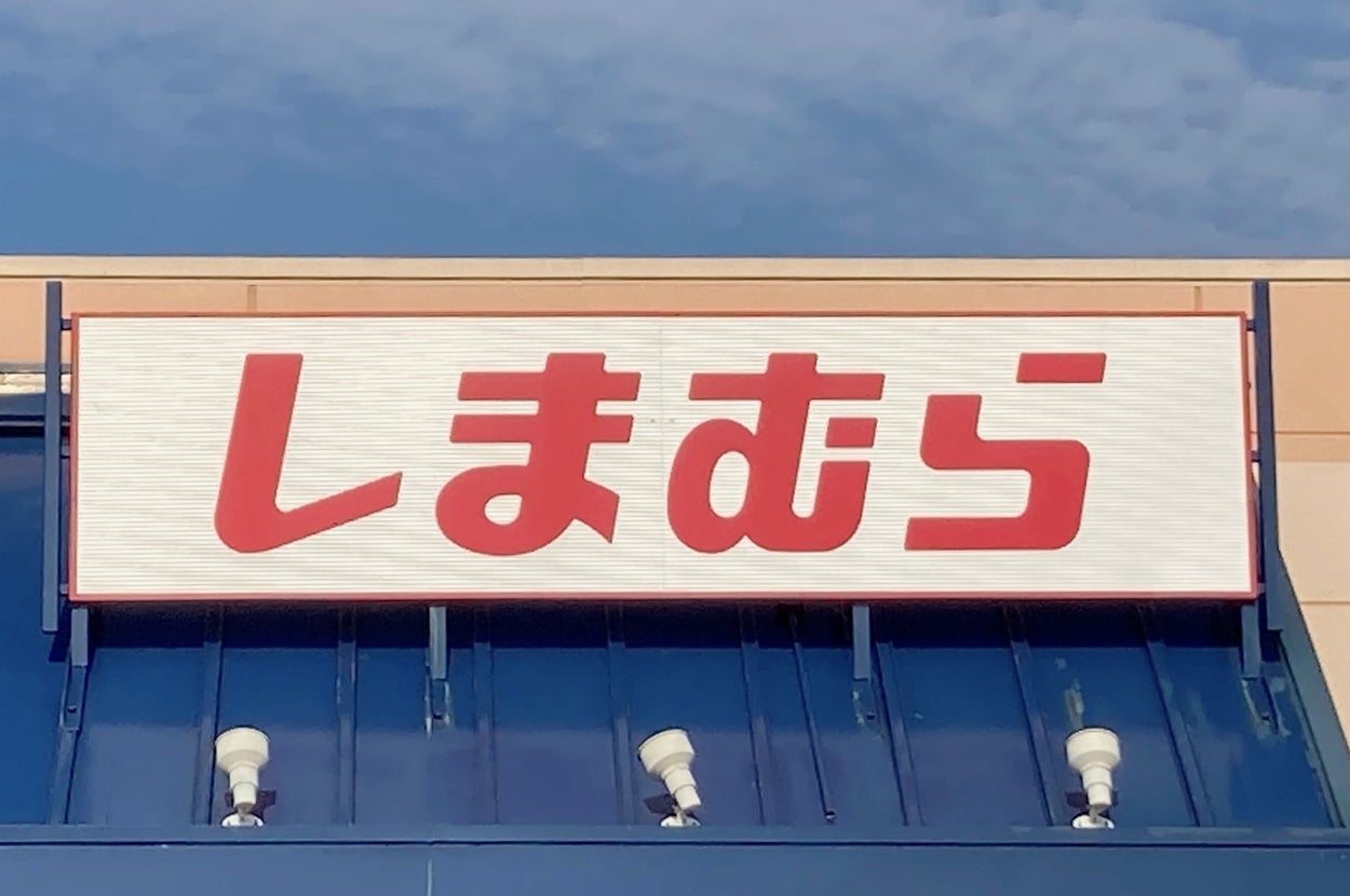 Storefront with a sign reading "しまむら" in Japanese above an entrance. Blue awning and a handicap parking sign in view