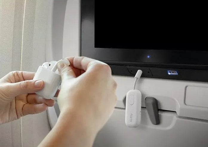 Tangan yang menghubungkan earbud nirkabel ke sistem hiburan dalam penerbangan menggunakan adaptor bluetooth