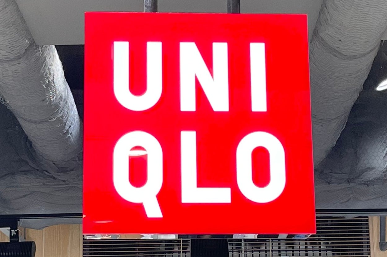 UNI QLO store sign hangs from the ceiling with merchandise shelves and price tags underneath