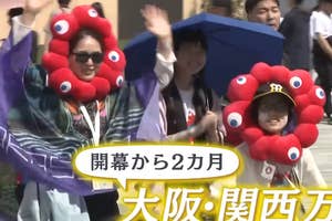 グループが大阪・関西万博でユニークな衣装を着てカメラに向かって手を振っている。