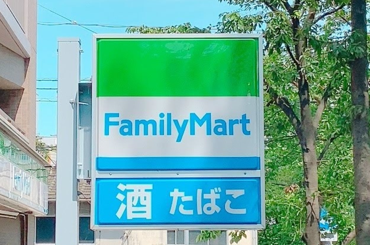ファミリーマートの看板。「酒」と「たばこ」の文字があり、緑の木々と青空が背景に見える。