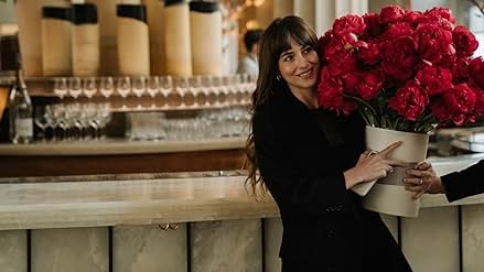 Person holding a large bouquet of red flowers, smiling in a modern setting with wine glasses in the background