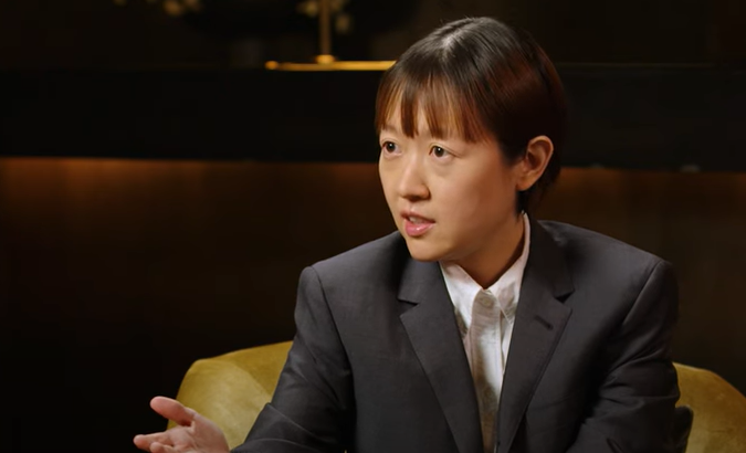 A person in a suit gestures while speaking in a formal setting