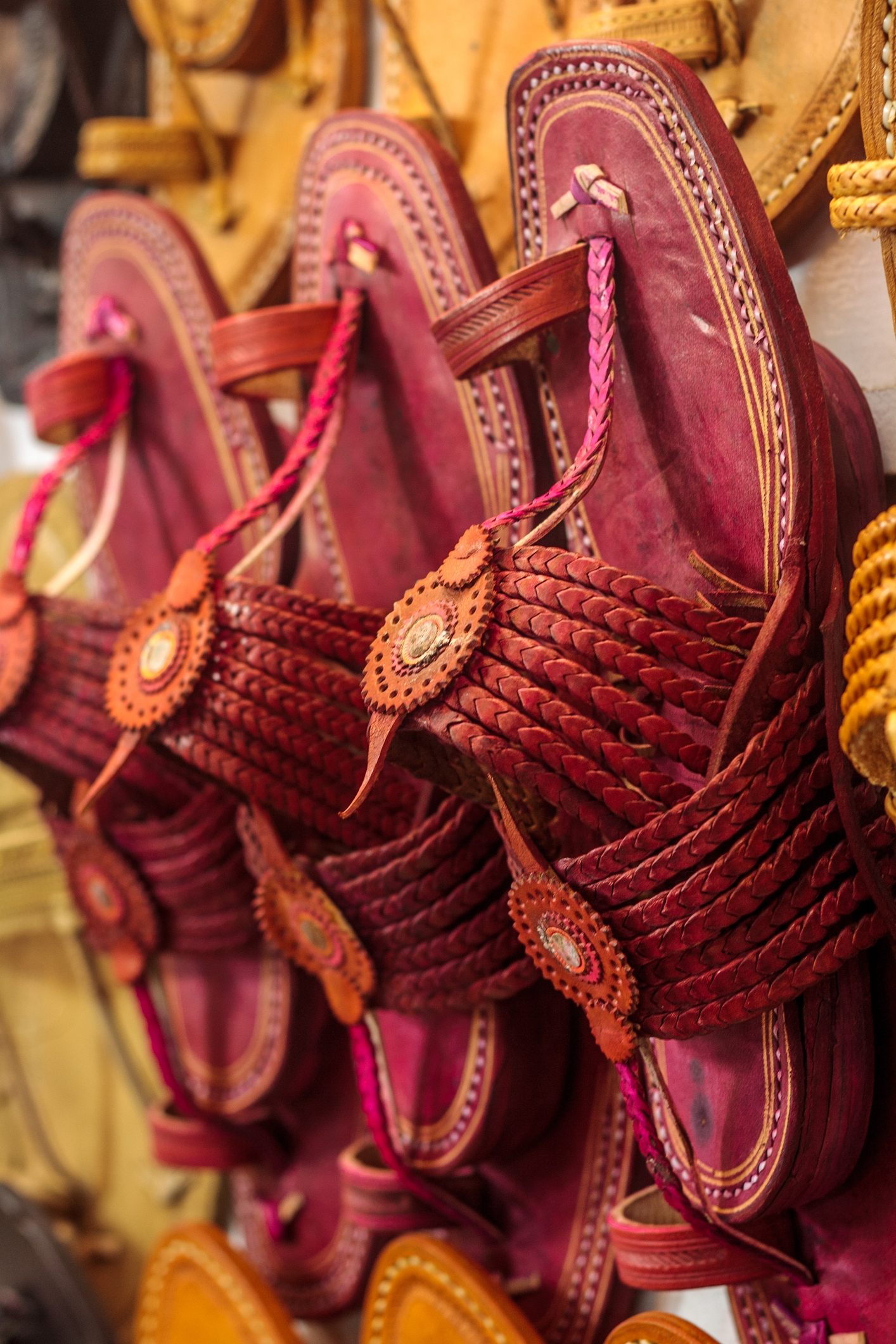 Handcrafted leather sandals with intricate braided straps and decorative circular accents displayed on a wall