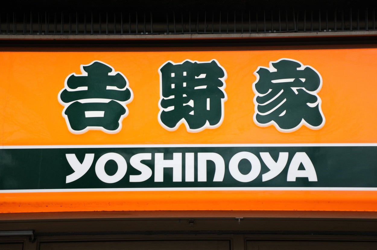 女性がレストランでラーメンを楽しんでいる様子。テーブル上に赤い小瓶があり、料理に用いている。