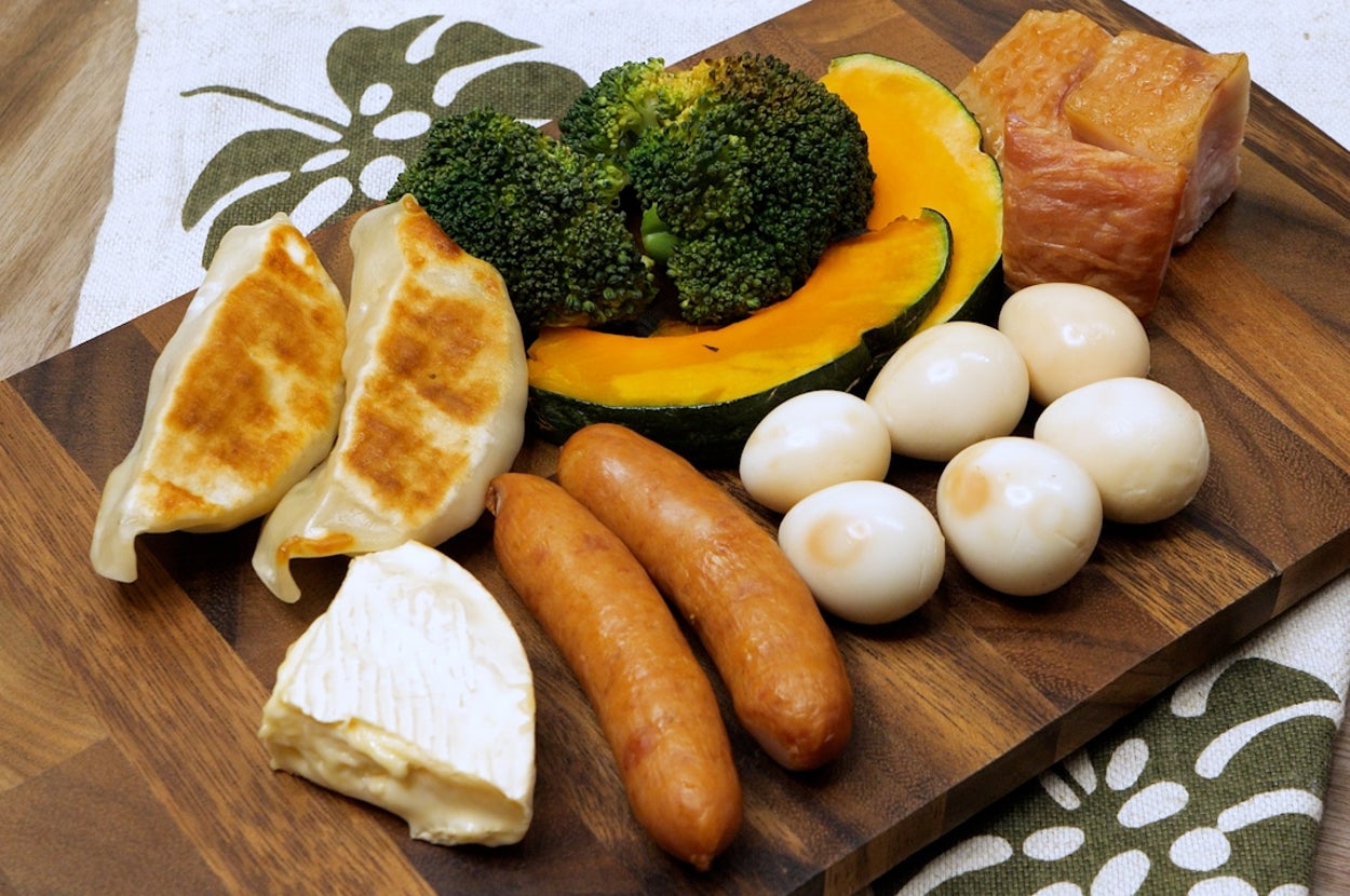 カッティングボードに餃子、ソーセージ、卵、ブロッコリー、かぼちゃ、肉が並べられている。