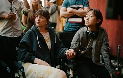 Two people hold hands seated on a set. One in a casual hoodie, the other with headphones, both with focused expressions
