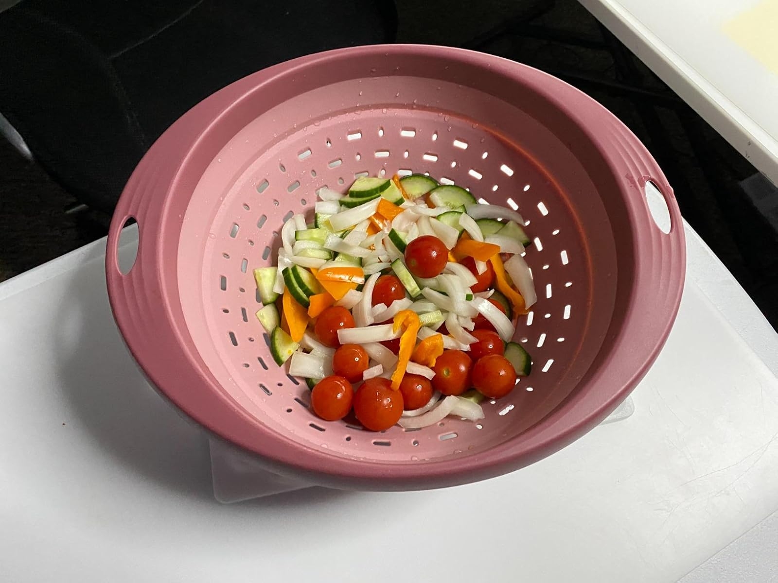 Reviewer's photo of fresh vegetables, including tomatoes, onions, and zucchini, in a pink colander on a table