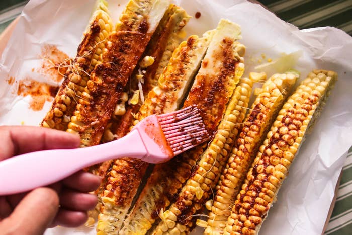 Corn connected  the cob seasoned with spices, being brushed with condiment  connected  a tray