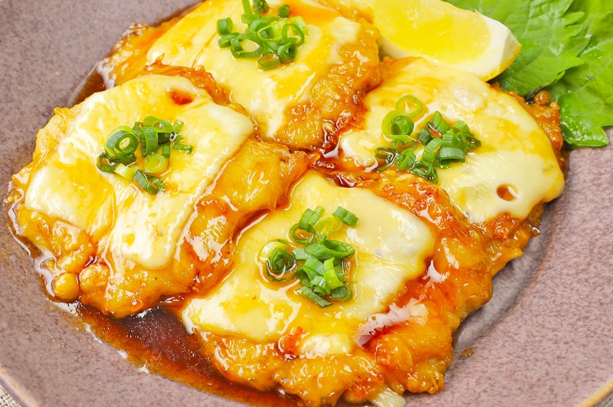 料理の皿にチーズとネギがかかっている焼き物が盛られており、レモンと葉が添えられている。