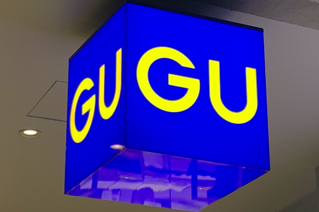 Sign displaying the letters "GU" in bold yellow on a blue cube, hanging from a ceiling