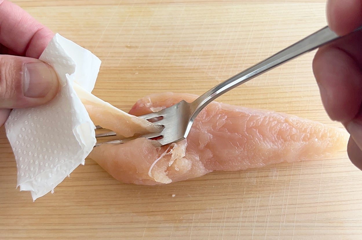 手でペーパータオルを使いフォークで押さえた生の鶏肉を裂いているシーン。