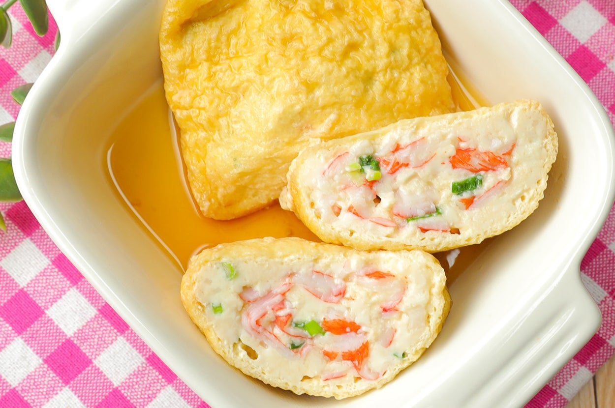 白い皿に入った焼き豆腐と野菜が詰まった揚げ物がピンクのチェック柄の布の上に置かれている。端に箸がある。