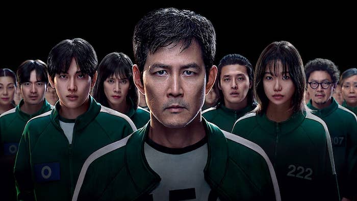 A group of serious-looking people in matching sportswear with numbers stand closely together, with one central figure at the forefront