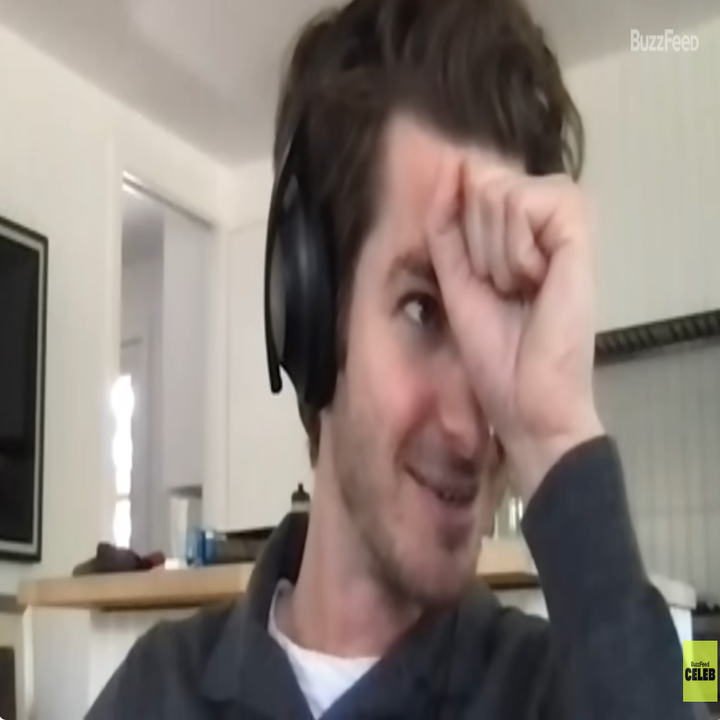 A person wearing headphones, sitting inside, smiling with the hand resting on the front. Unofficially visible clothes