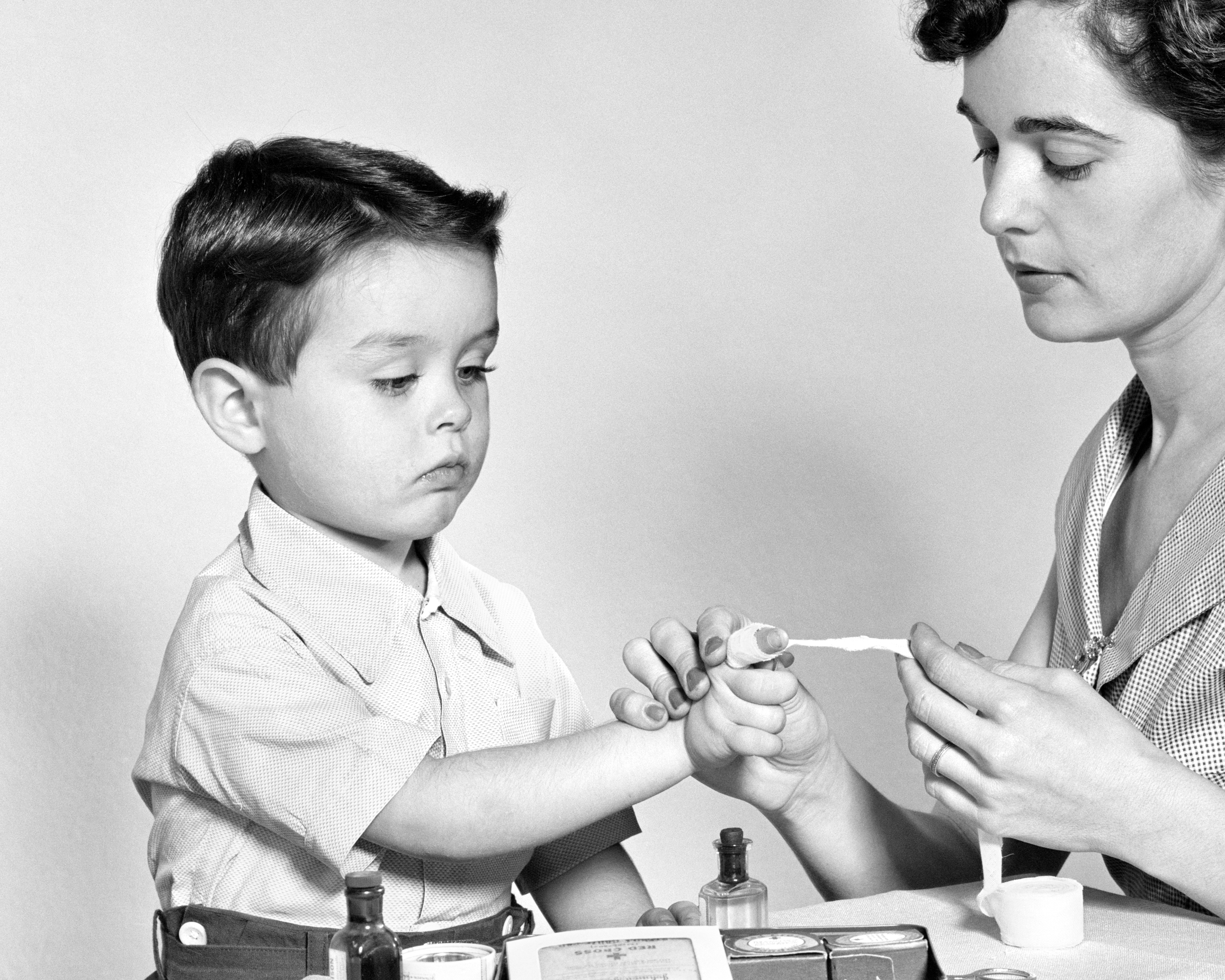 En kvinne bruker nøye neglelakk på en ung guttes hånd, begge fokuserte på aktiviteten, med små flasker og verktøy på bordet