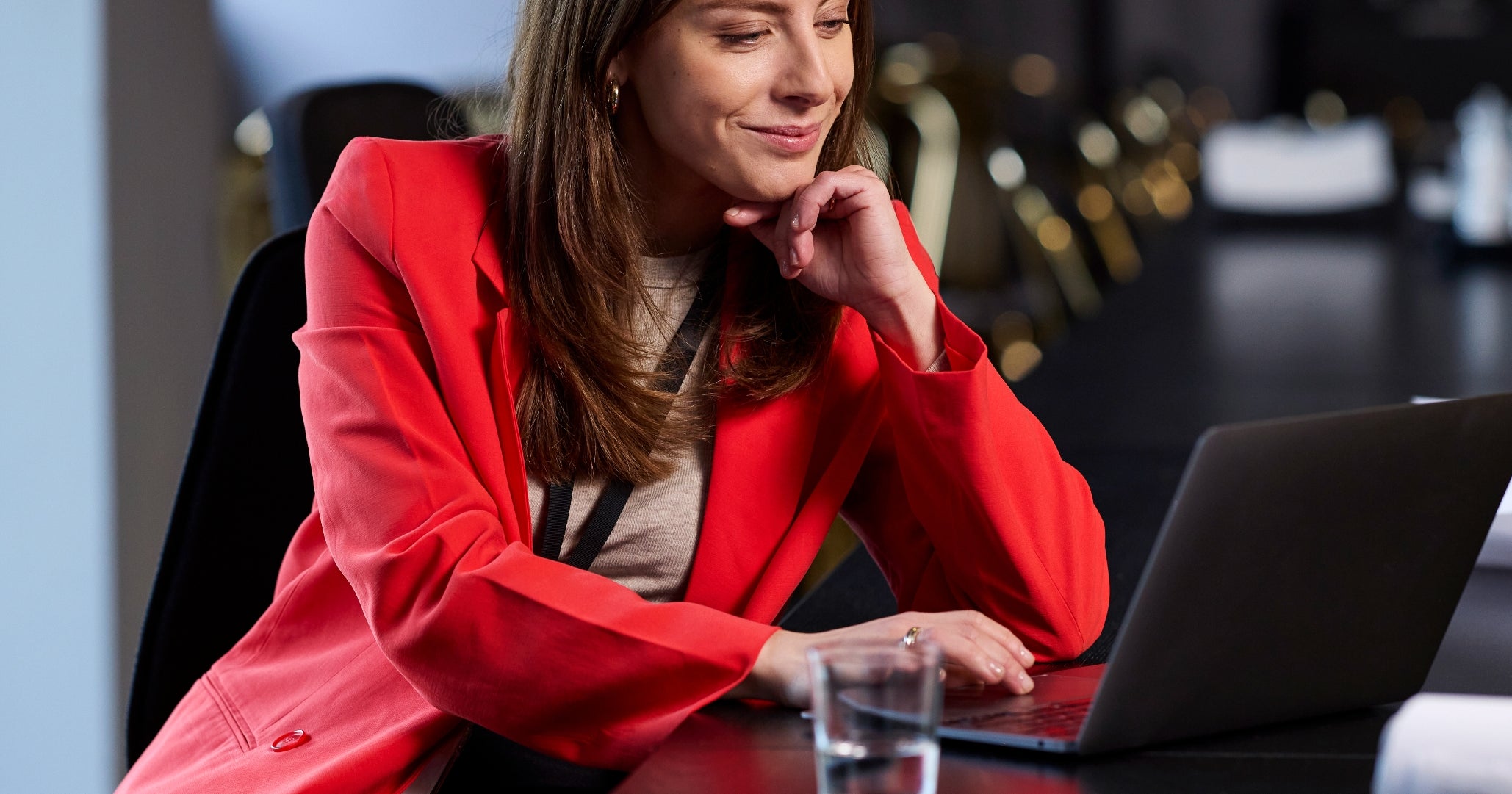 Kvinne i en rød blazer som jobber med en bærbar datamaskin ved et langt konferansebord med tegninger i nærheten