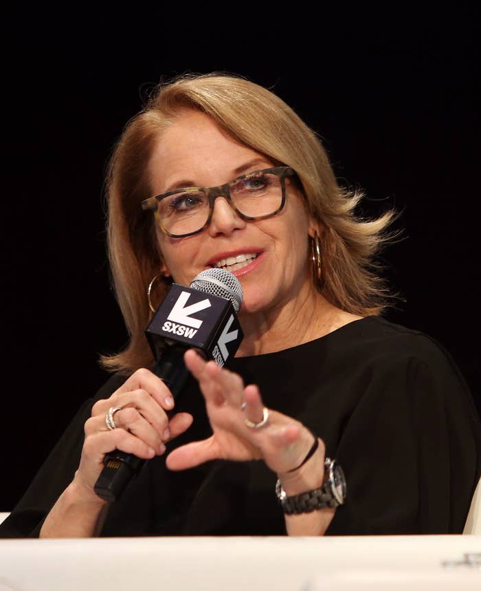 Katie Couric with glasses, in a outfit, speaks animatedly into a microphone marked &quot;SXSW&quot; during a discussion or panel event