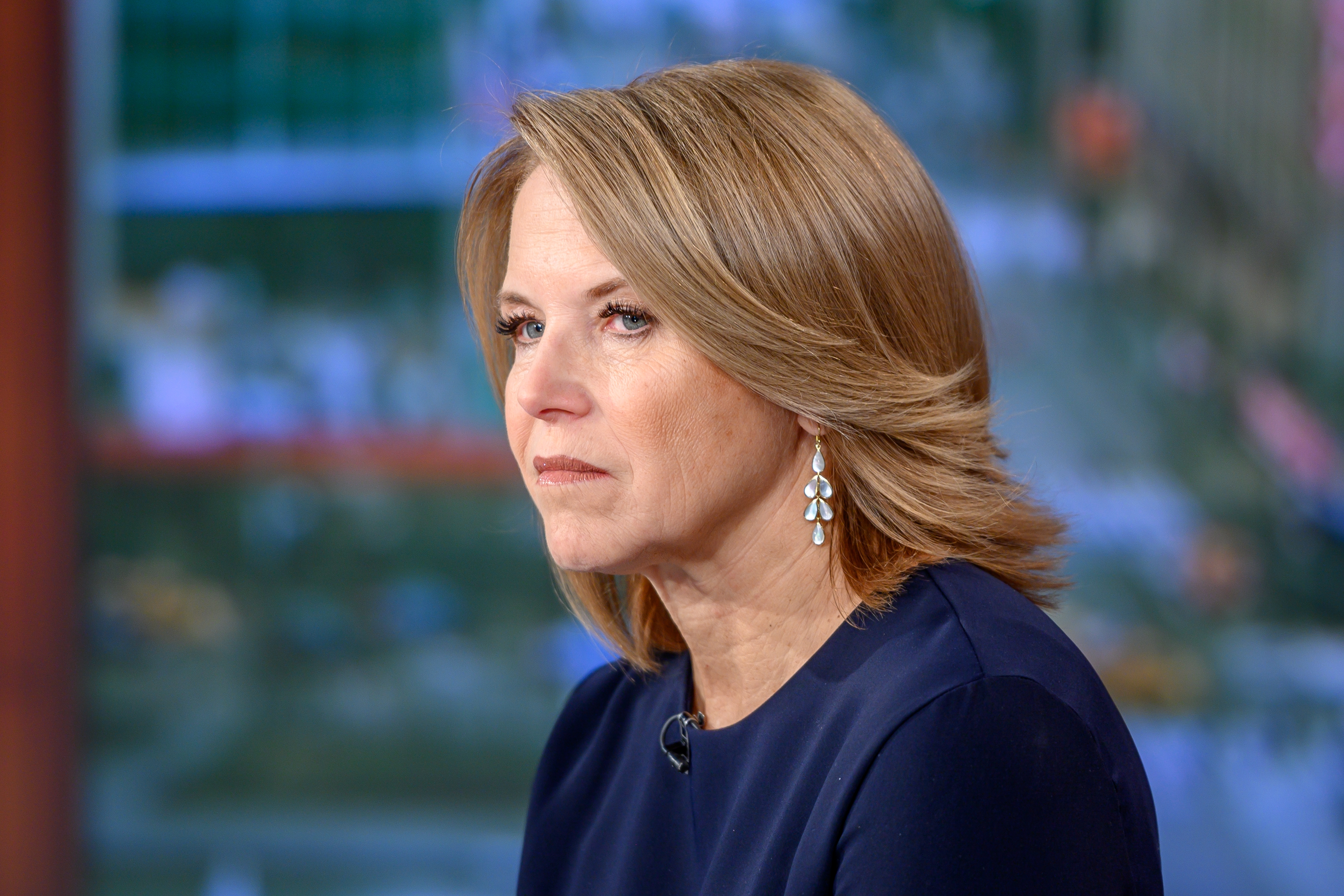 Katie Couric with shoulder-length hair and drop earrings in a studio setting, gazing thoughtfully ahead