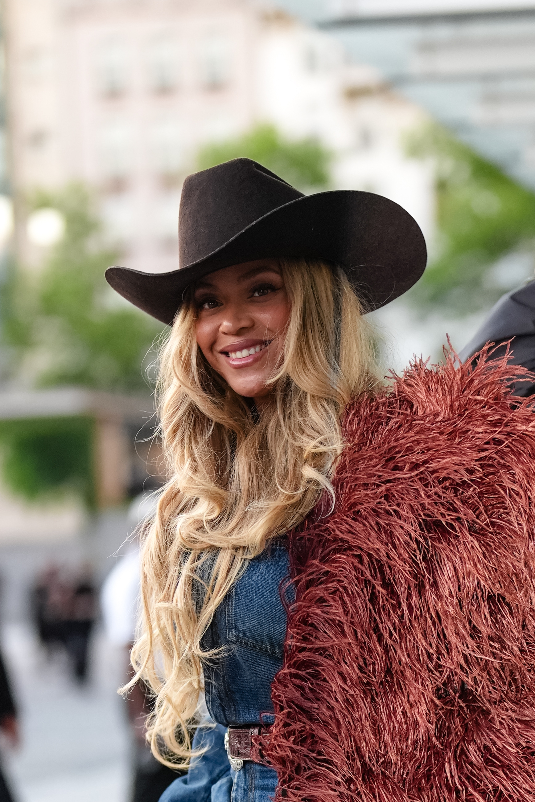 Person in a cowboy hat and textured jacket smiles outdoors