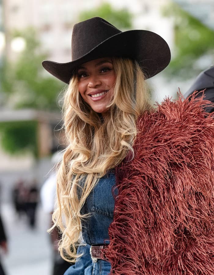 Person in a cowboy hat and textured jacket smiles outdoors