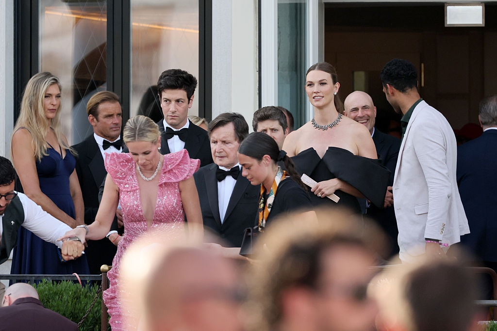 Group of people in formal attire at an event; a woman in off-shoulder black dress is prominent