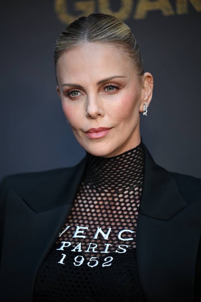 Person in a stylish, tailored black blazer over a mesh top with text, on a formal event backdrop