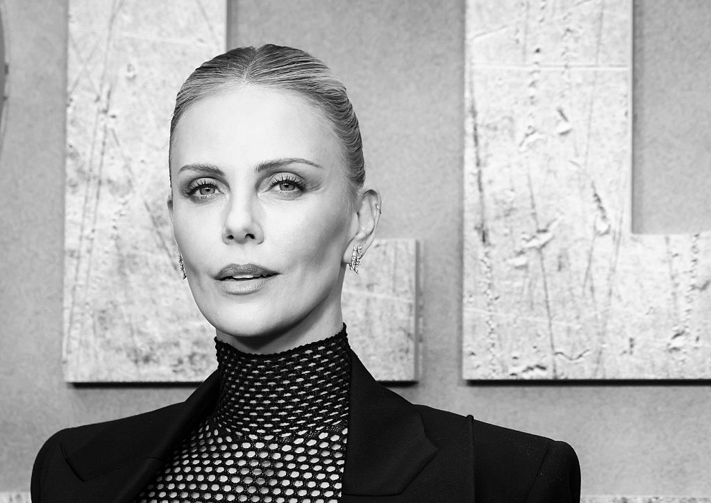Person with slicked-back hair in a high-neck patterned top and blazer, posing for a formal event photo